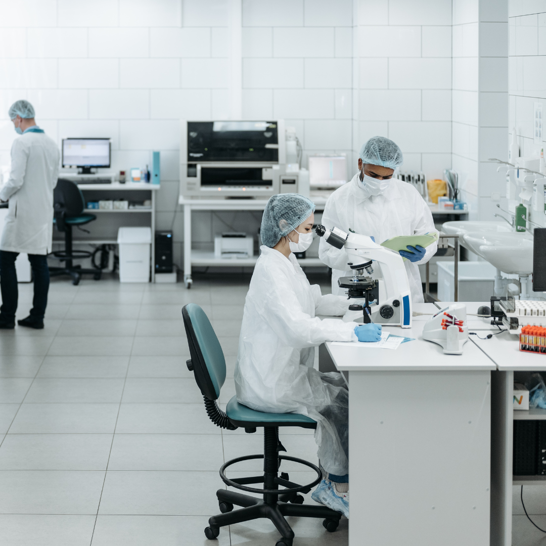 Imagen de un laboratorio moderno donde se desarrollan productos de cosmética natural. Se observa a un investigador utilizando un microscopio, mientras otro revisa documentos. El entorno es limpio y organizado, reflejando un enfoque profesional en la investigación y desarrollo de cosméticos saludables y efectivos.